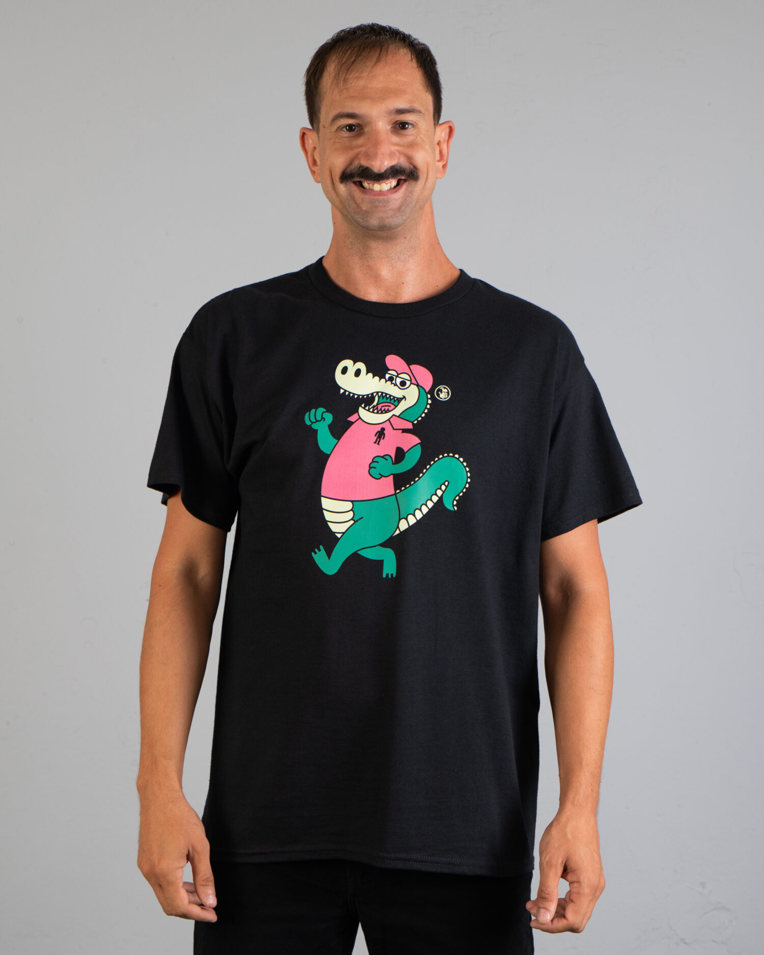 Czarna koszulka marki Dziedzic Pruski z autorską grafiką nawiązująca do stylistyki marki Lacoste i logo z krokodylkiem lub aligatorem. Przedstawia wesołego krokodyla paradującego w koszulce z kołnierzykiem typu polo oraz emblematem postaci ludzkiej. Ta zabawna koszulka nie posiada żadnego napisu. Jest bez napisów.