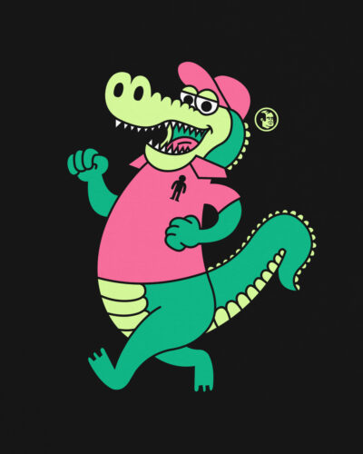 Czarna koszulka marki Dziedzic Pruski z autorską grafiką nawiązująca do stylistyki marki Lacoste i logo z krokodylkiem lub aligatorem. Przedstawia wesołego krokodyla paradującego w koszulce z kołnierzykiem typu polo oraz emblematem postaci ludzkiej. Ta zabawna koszulka nie posiada żadnego napisu. Jest bez napisów.